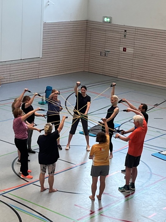 Gymnastikgruppe mit Theraband im Kreis in der Halle